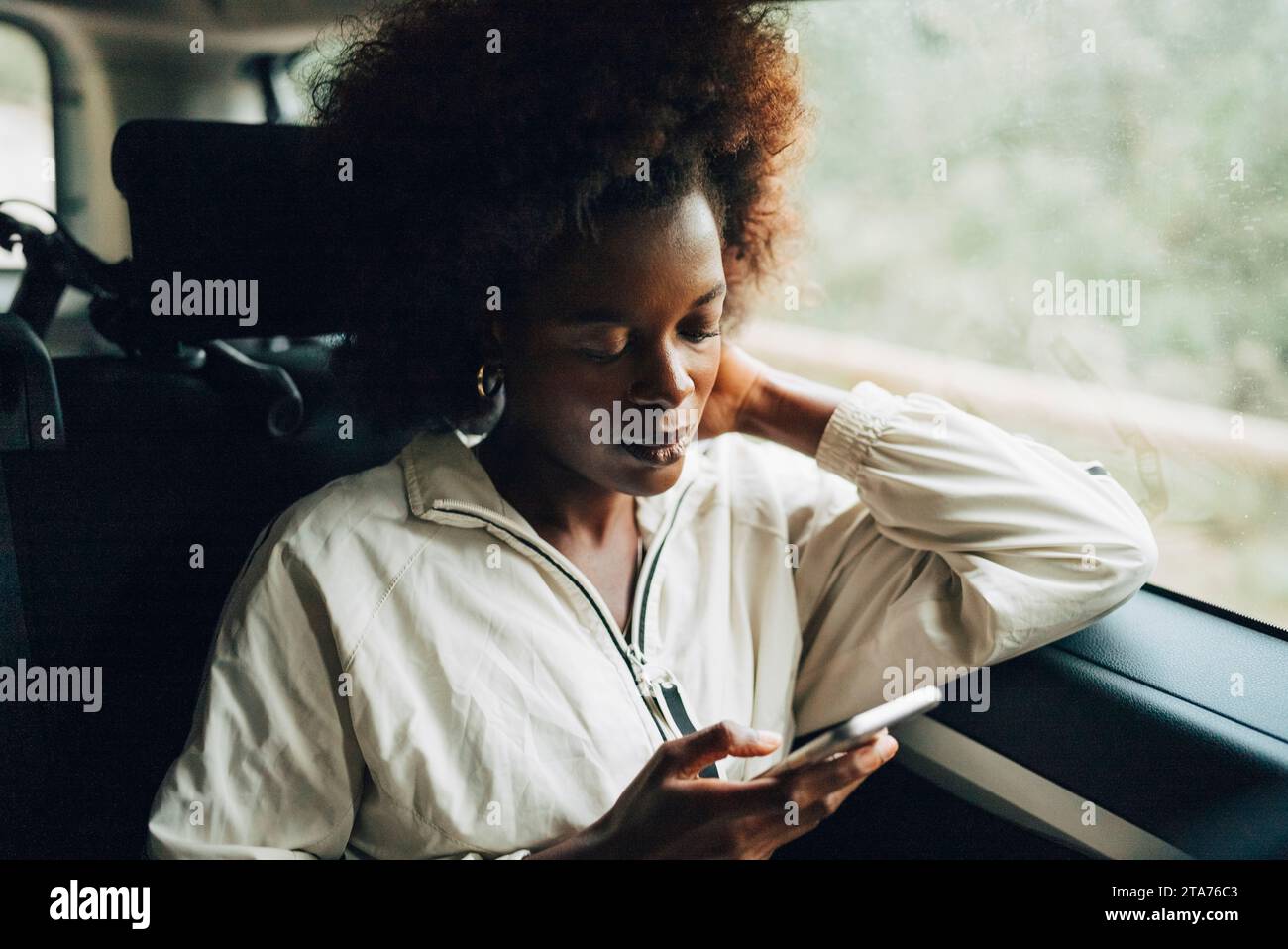 Junge Afro-Frau, die ihr Smartphone benutzt, während sie während der Fahrt im Van sitzt Stockfoto