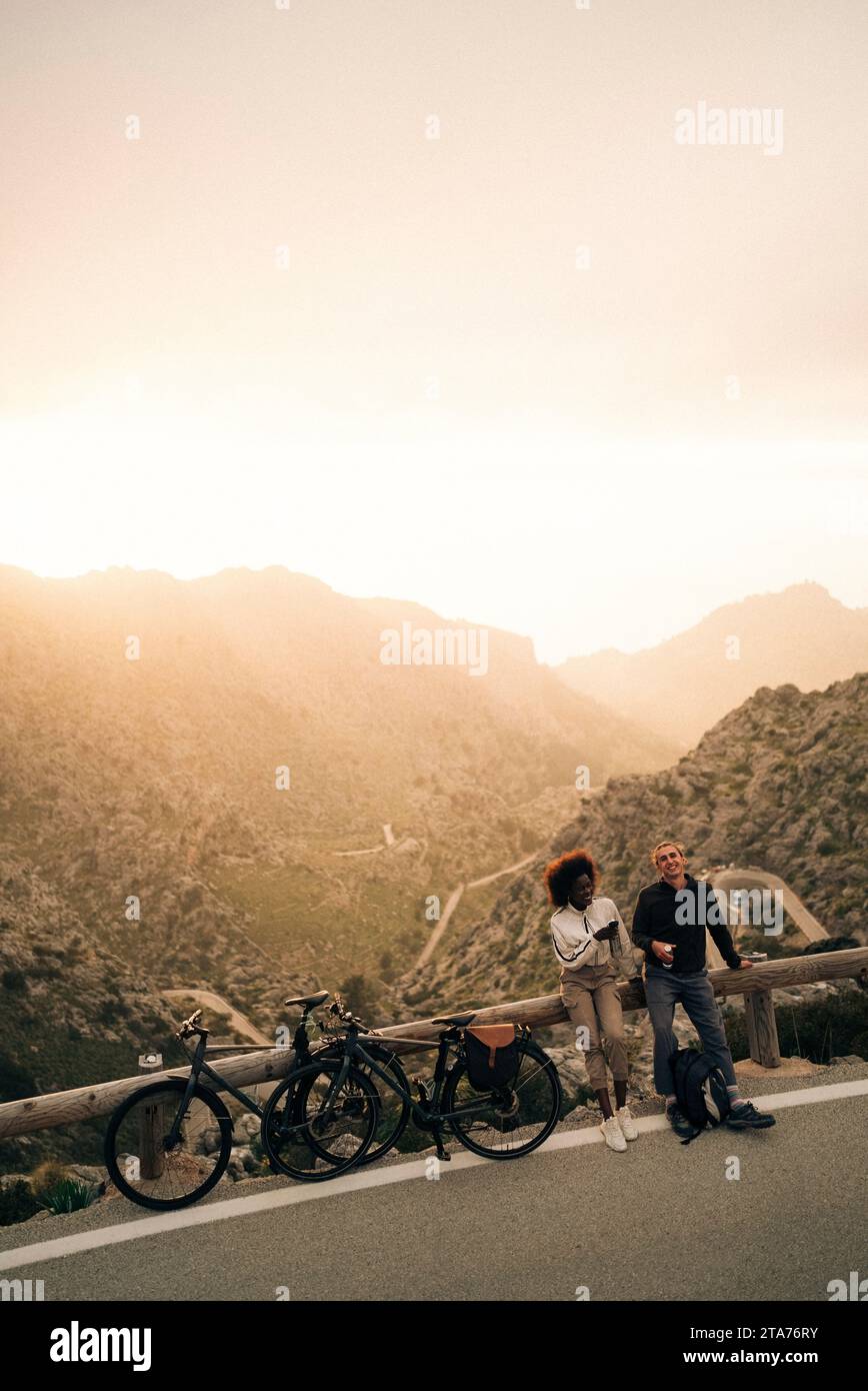 Mann und Frau mit Fahrrädern stehen am Straßenrand bei Sonnenuntergang im Urlaub Stockfoto