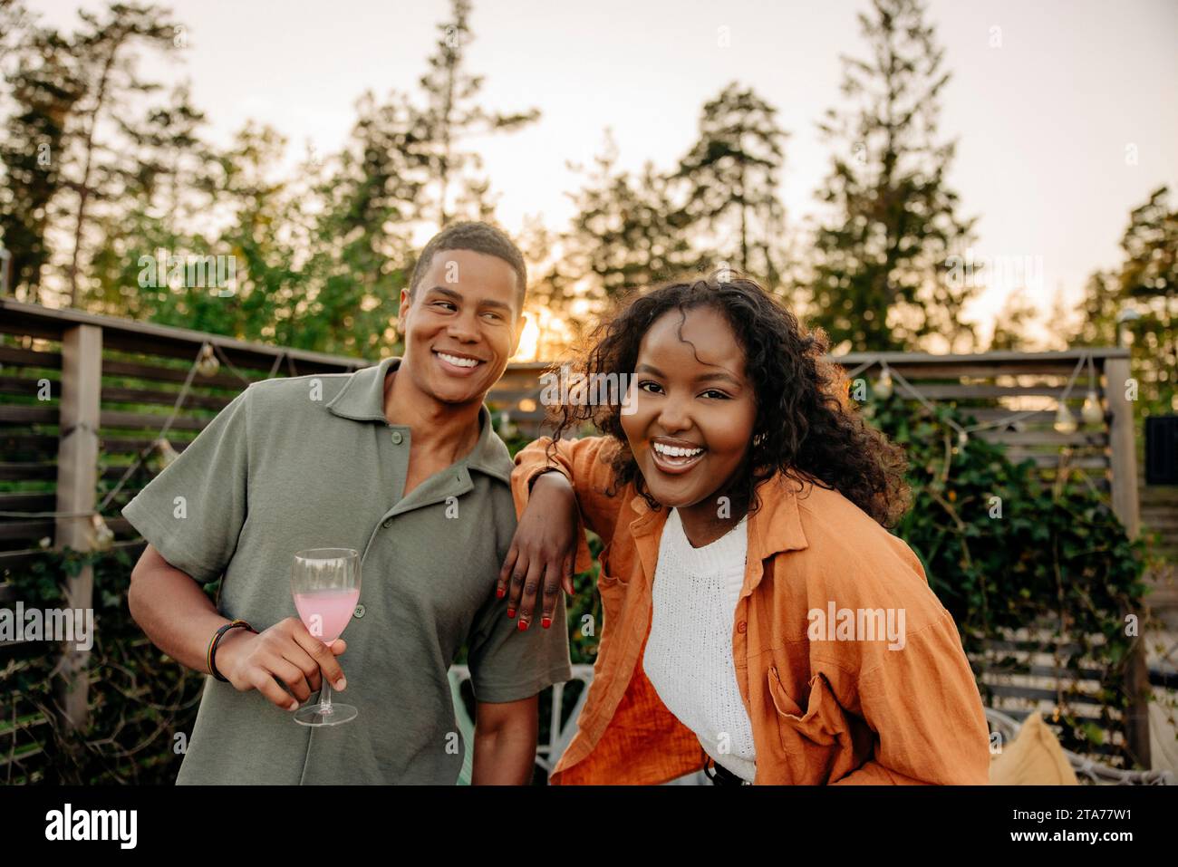 Porträt einer glücklichen Frau mit Hand auf der Schulter eines männlichen Freundes, der bei der Dinnerparty ein Glas hält Stockfoto