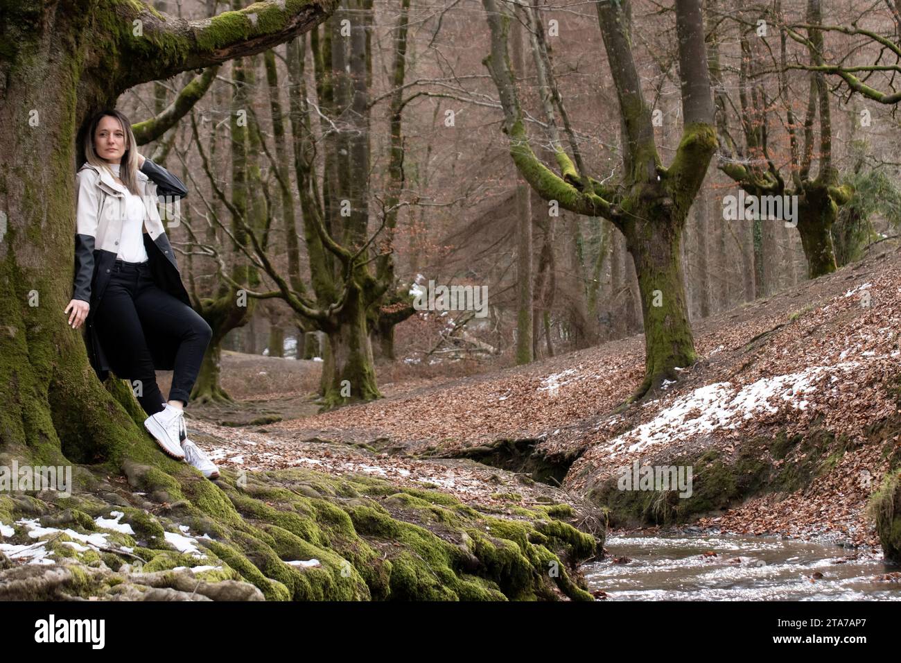 Frau auf einem moosbedeckten Baumzweig in einem Wald, mit einem Fluss im Hintergrund Stockfoto