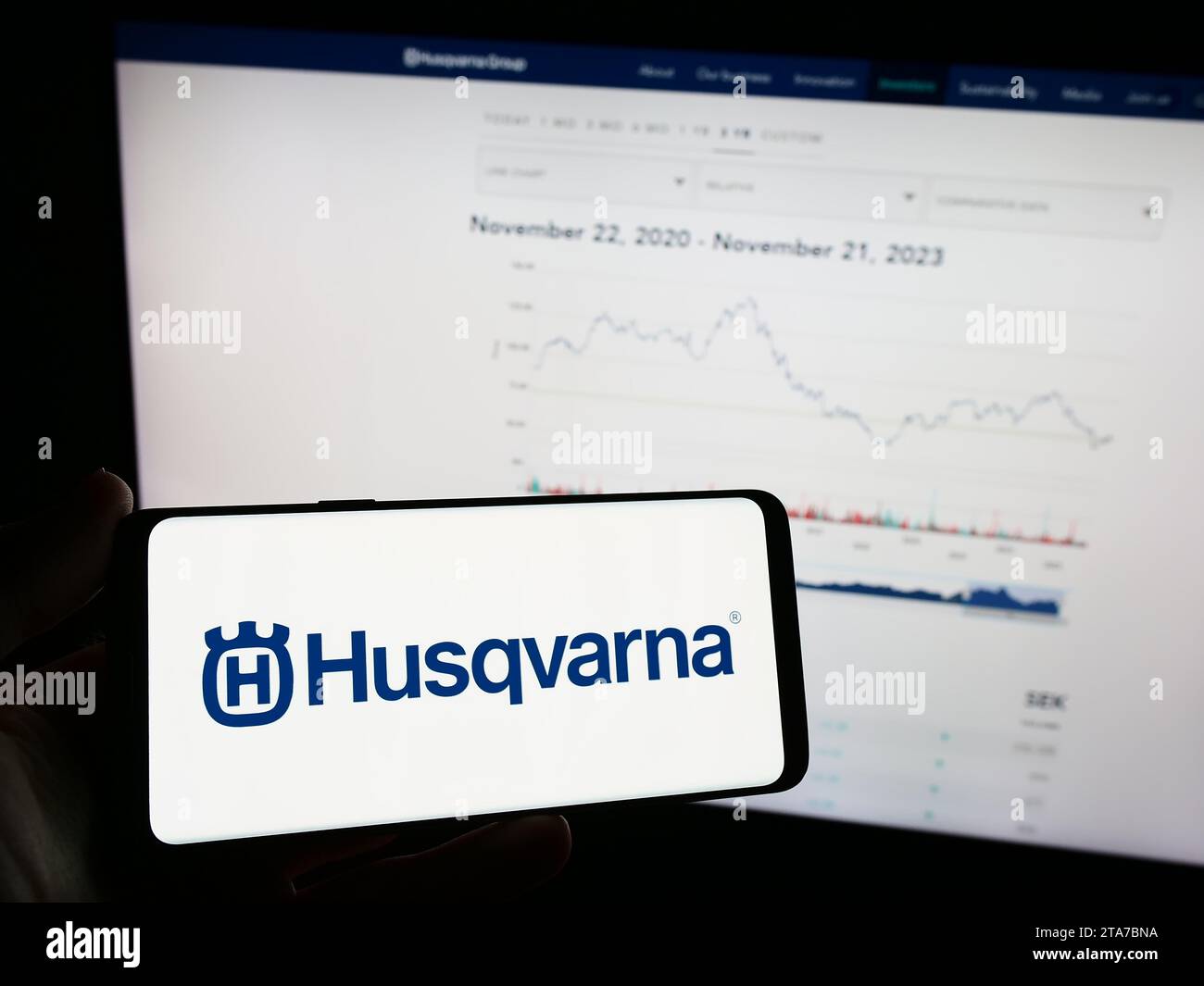 Person, die ein Mobiltelefon mit dem Logo des schwedischen Energieunternehmens Husqvarna ab vor der Webseite des Unternehmens hält. Schwerpunkt auf dem Display des Telefons. Stockfoto