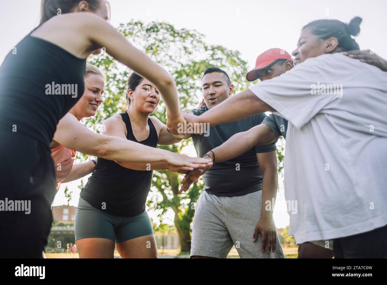 Niedriger Blickwinkel auf männliche und weibliche Freunde, die während des Trainings im Park Hände stapeln Stockfoto