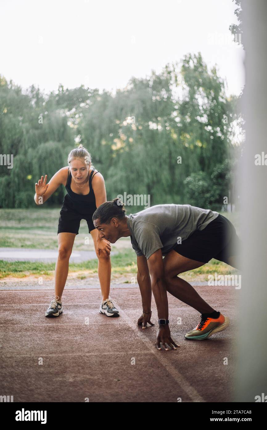 Weibliche Trainerin, die dem Mann bei der Vorbereitung auf den Sprint auf der Laufbahn hilft Stockfoto