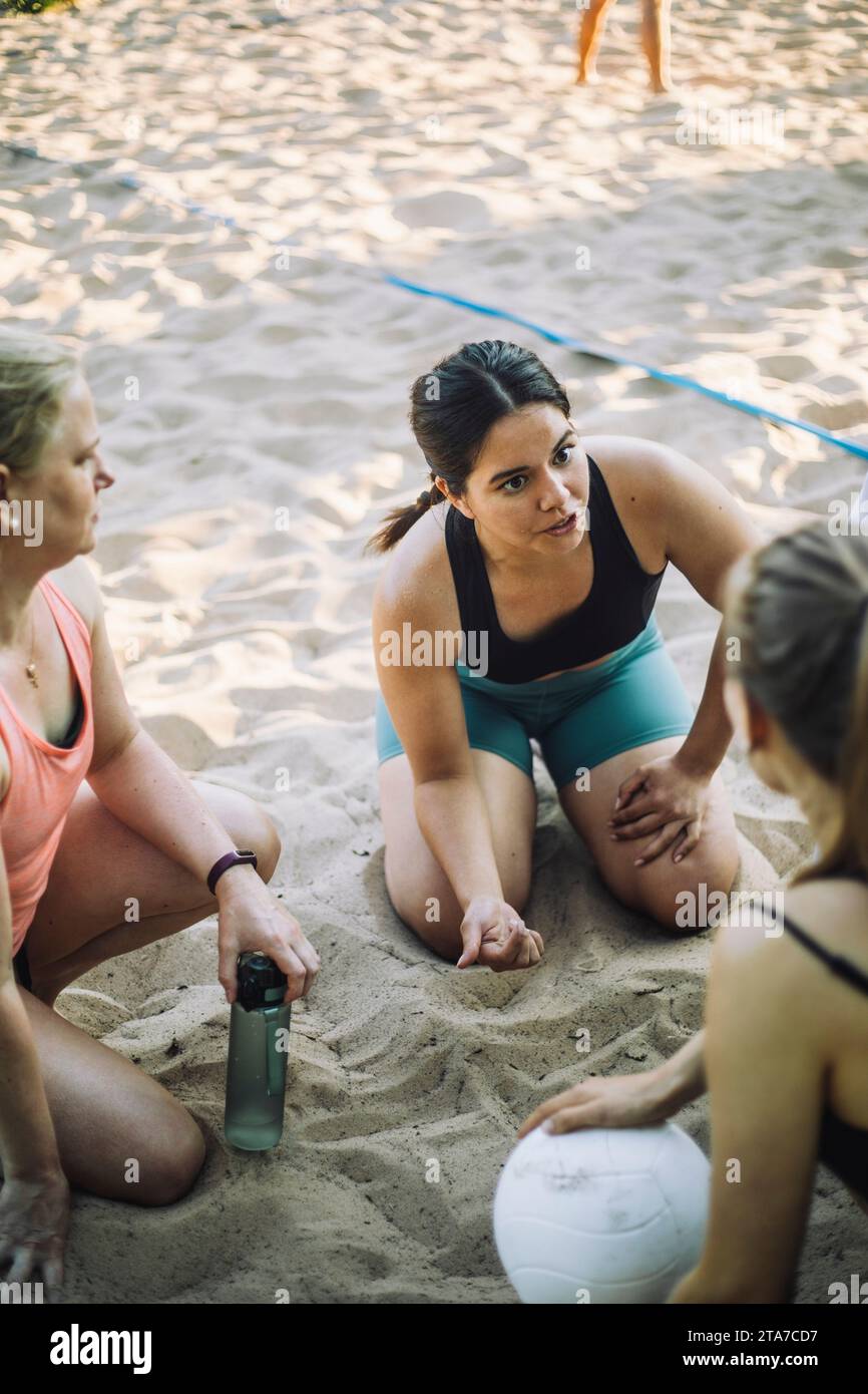 Frau, die mit einem Freund spricht, der Volleyball auf Sand hält Stockfoto