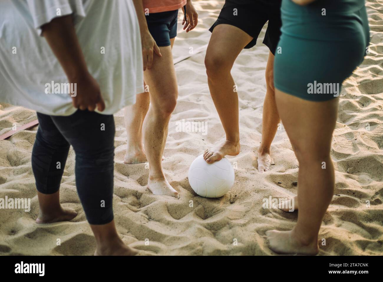 Niedriger Teil von Freundinnen, die mit Volleyball auf Sand stehen Stockfoto