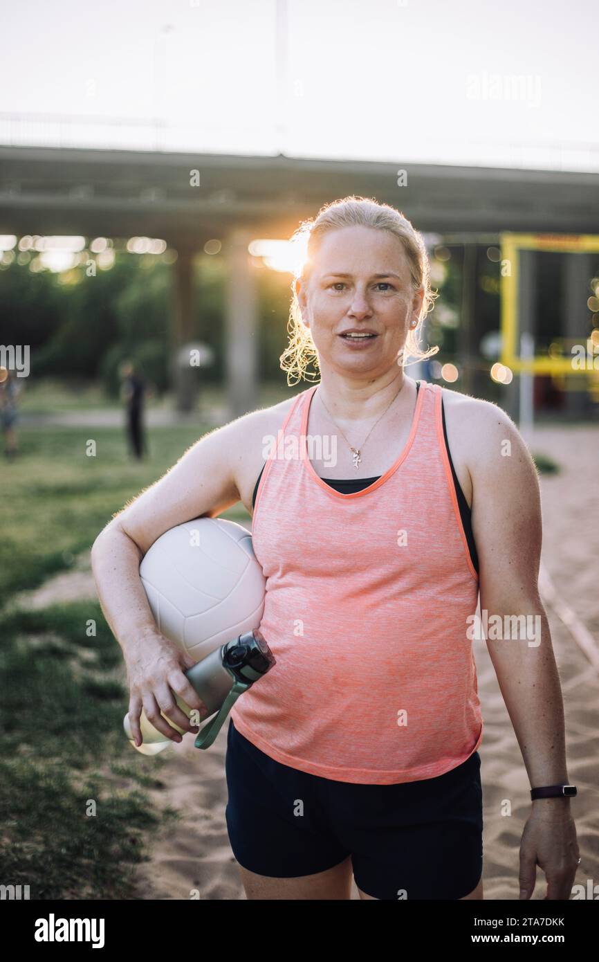 Porträt einer Frau, die Wasserflasche und Volleyball unter dem Arm hält Stockfoto