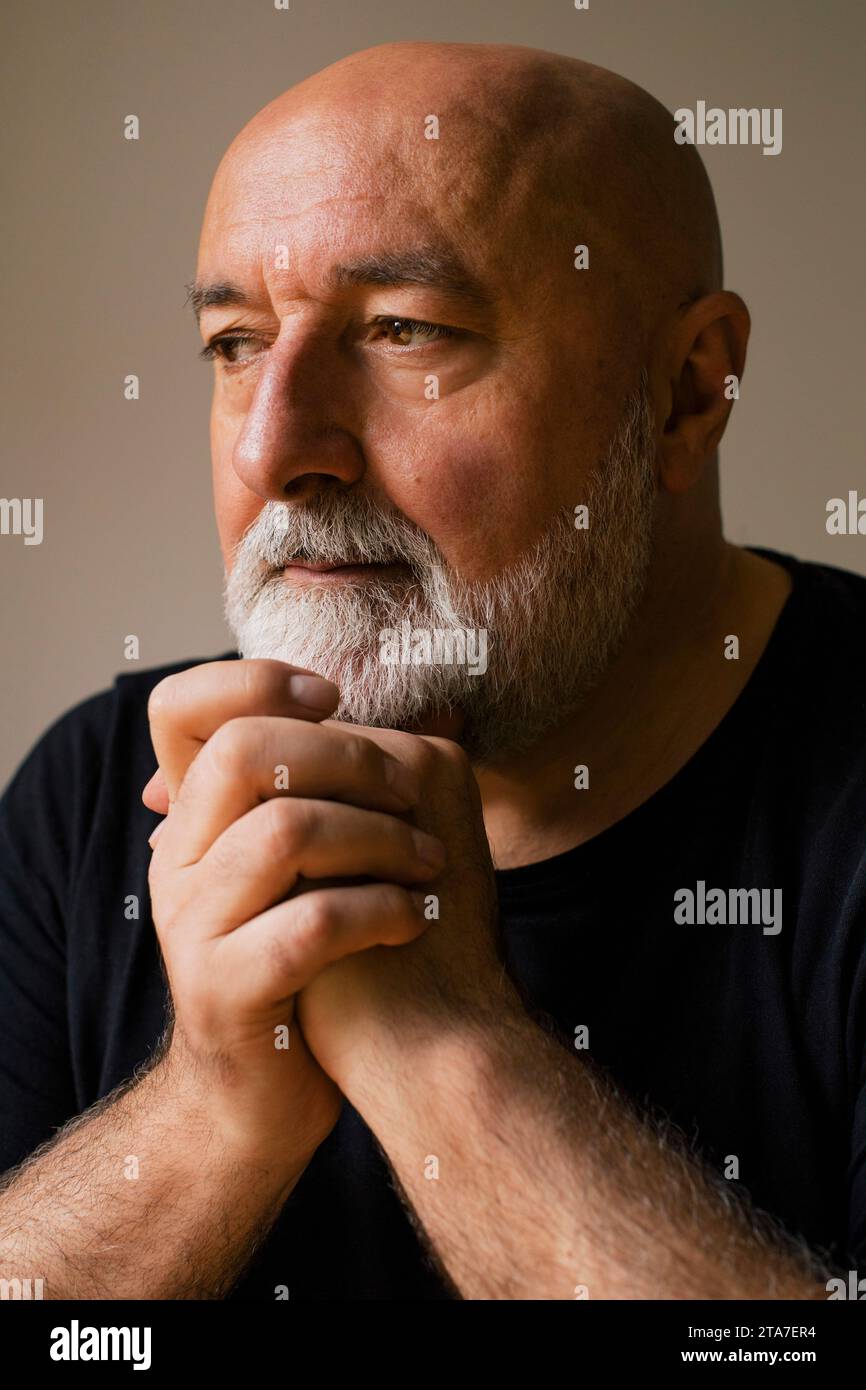 Ernster reifer Mann mit gefesselten Händen, der zu Hause nachdenkt Stockfoto