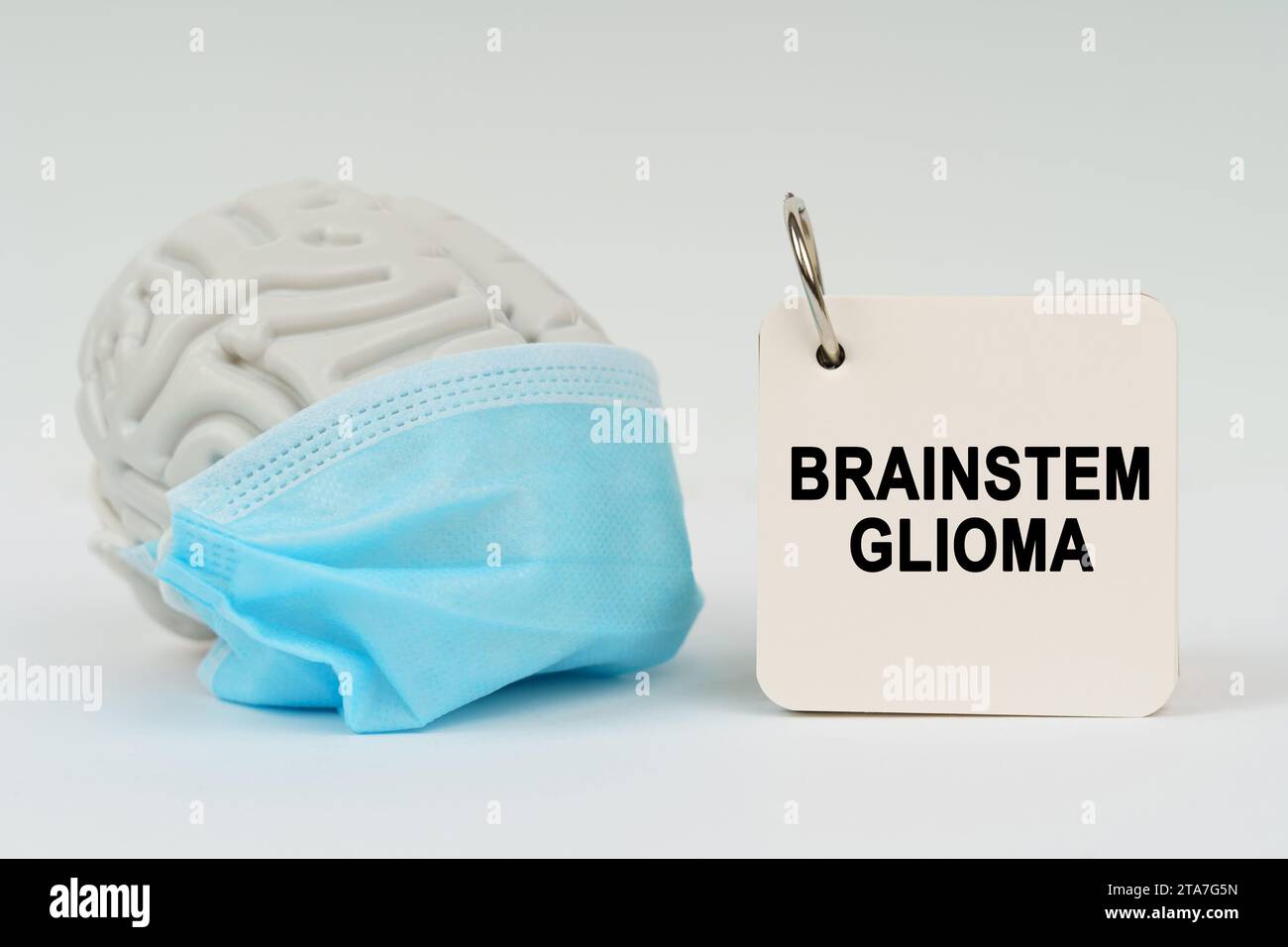 Medizinisches Konzept. Auf einer weißen Oberfläche befindet sich ein Gehirn mit einer blauen Maske und ein Notizblock mit der Inschrift - Hirnstamm Gliom Stockfoto