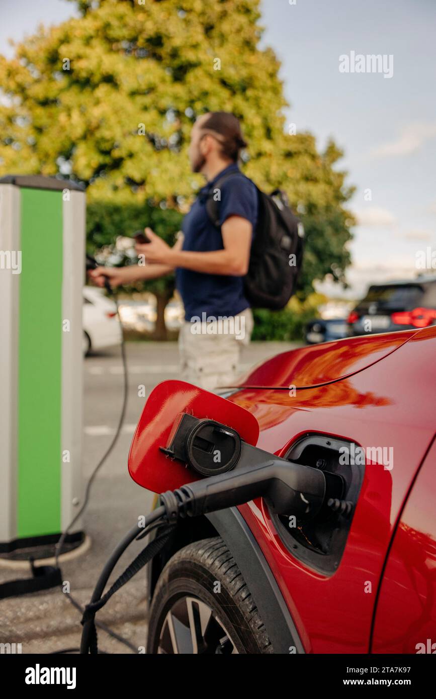 Elektrokabel, das das Auto auflädt, während ein Mann im Hintergrund auf der Station steht Stockfoto