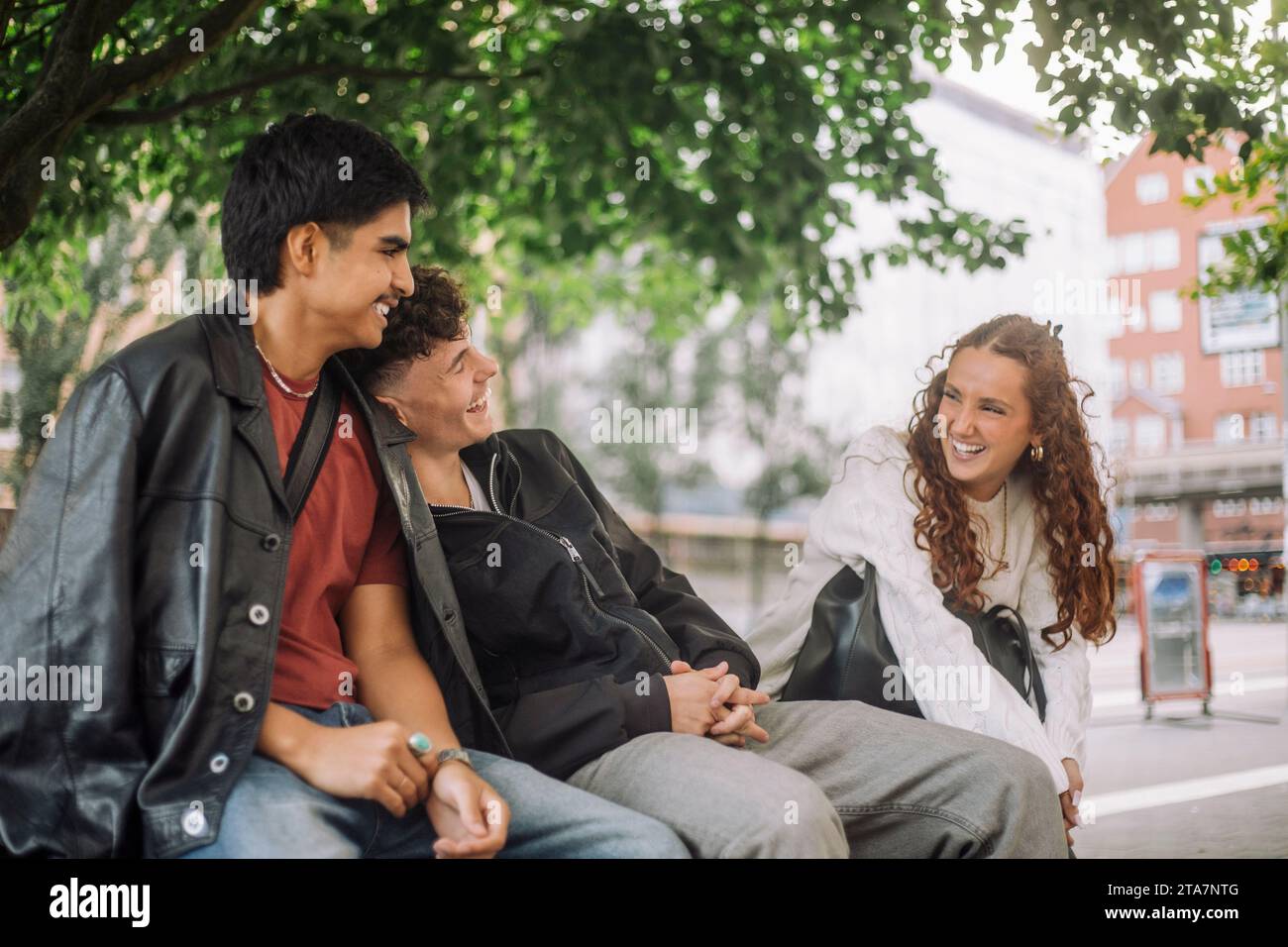 Teenager, männliche und weibliche Freunde, die zusammen lachen, während sie auf der Bank sitzen Stockfoto