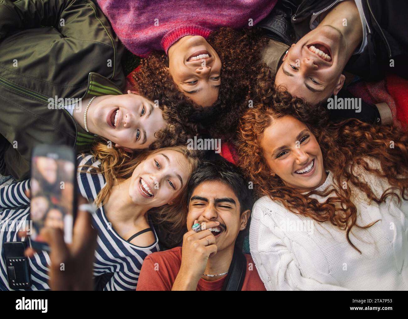 Hand einer nicht erkennbaren Person, die fröhliche Teenager-Freunde fotografiert und Spaß beim Liegen im Park hat Stockfoto
