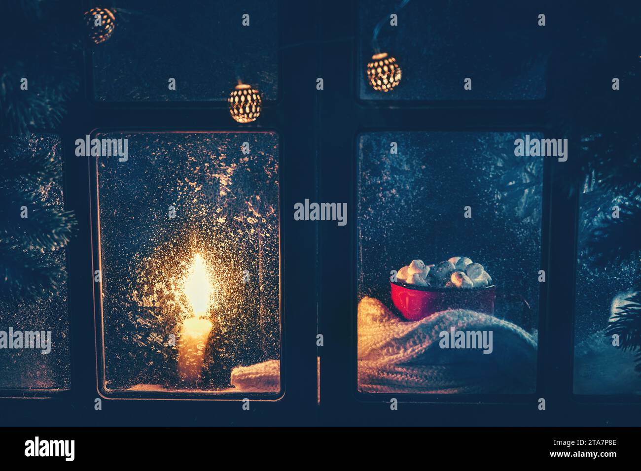 Weihnachten, Neujahr, Winterkomposition. Roter Becher mit Kakao und Marshmallows und Kerze hinter einem gefrorenen Fenster mit frostigen Mustern Stockfoto