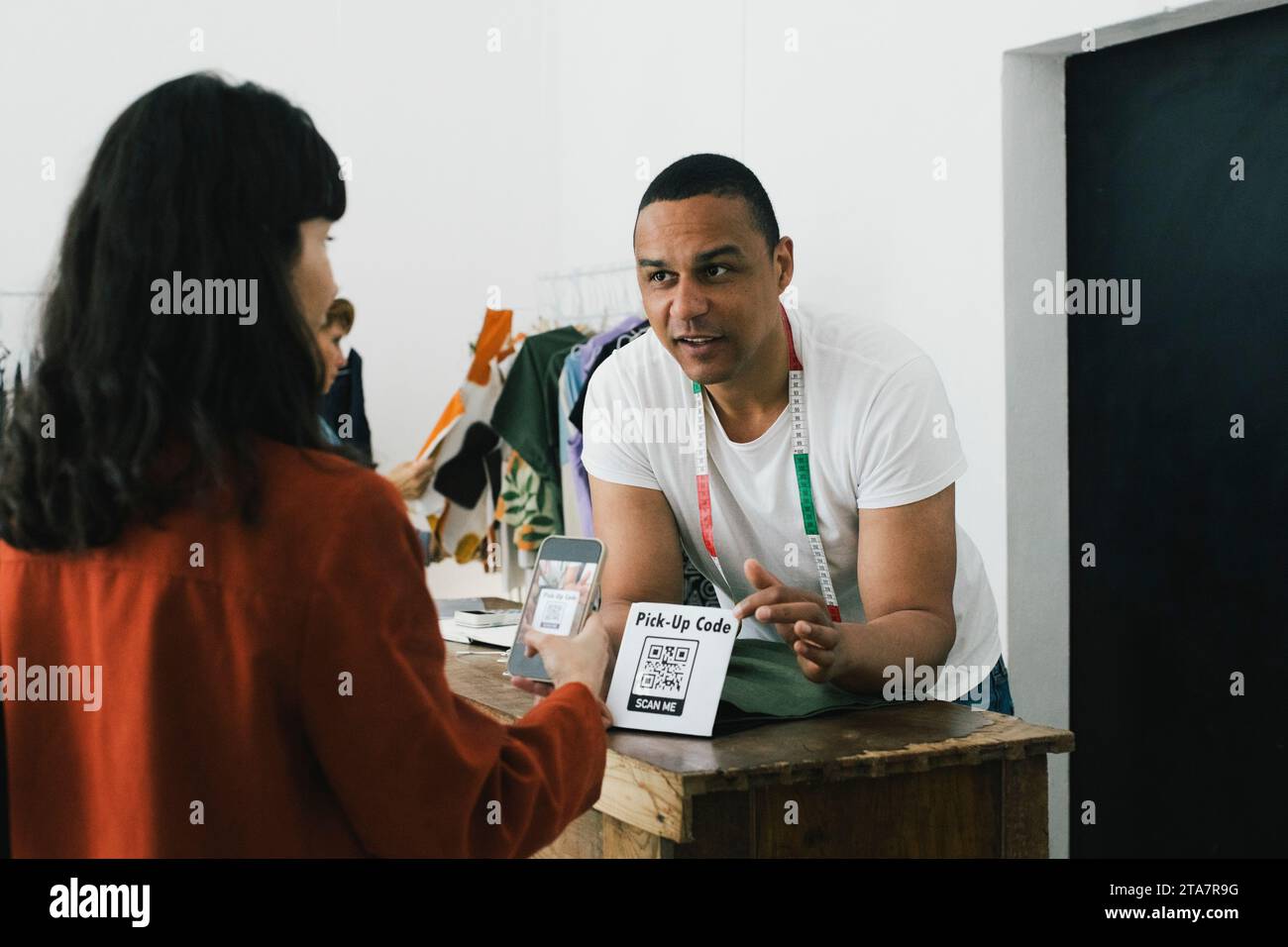 Der Schneider zeigt auf den Barcode-Scanner, während er mit dem Kunden im Geschäft spricht Stockfoto