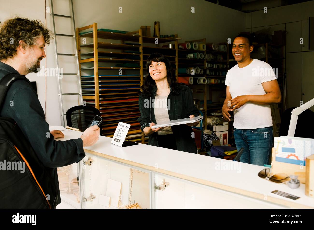 Lächelnde Techniker geben dem Kunden, der im Geschäft bezahlt, einen gewarteten Laptop Stockfoto