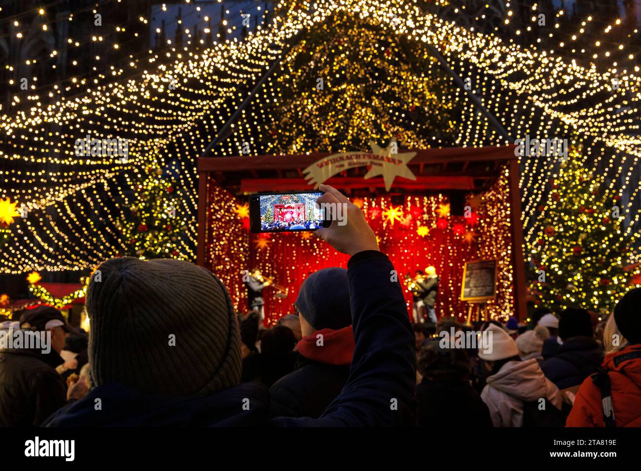 Bühne auf dem Weihnachtsmarkt am Roncalliplatz vor dem Dom, Mann fotografiert mit seinem Smartphone, Köln, Deutschland. Buehne auf dem We Stockfoto