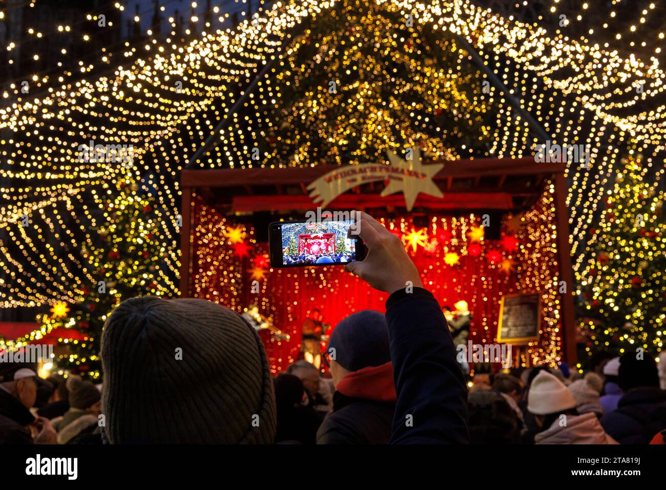 Bühne auf dem Weihnachtsmarkt am Roncalliplatz vor dem Dom, Mann fotografiert mit seinem Smartphone, Köln, Deutschland. Buehne auf dem We Stockfoto