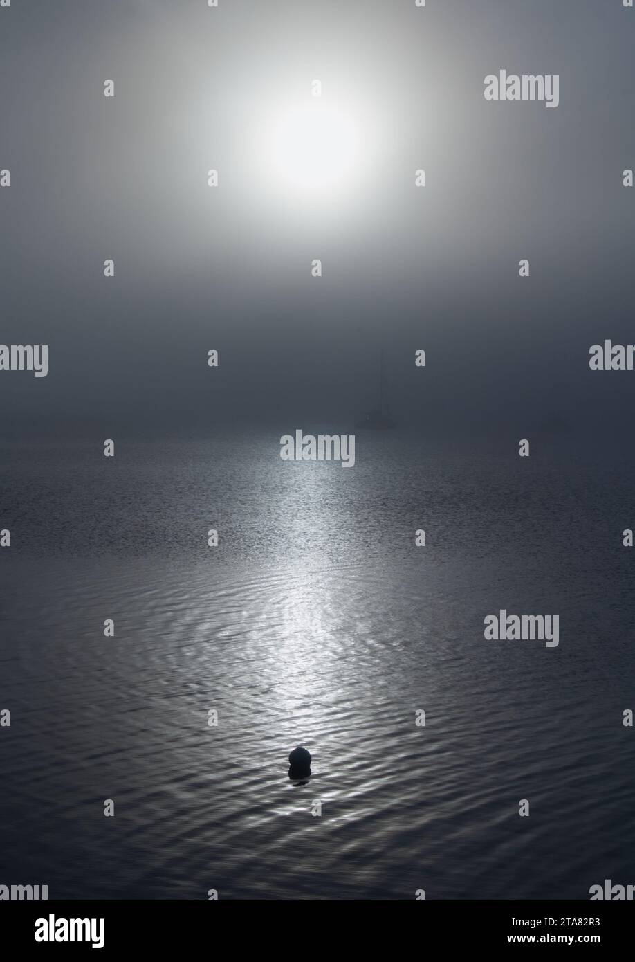 Boje beleuchtet von der Sonne mit Sea Fog, Haar oder Sea Fret mit ruhigem Wasser, Christchurch Harbour, Großbritannien Stockfoto