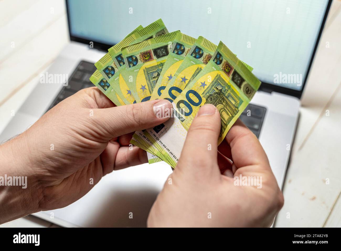24. November 2023: Ein Mann hält mehrere 100-Euro-Banknoten vor seinem Laptop *** ein Mann hält mehrere 100 Euro Geldscheine vor seinem Laptop Credit: Imago/Alamy Live News Stockfoto