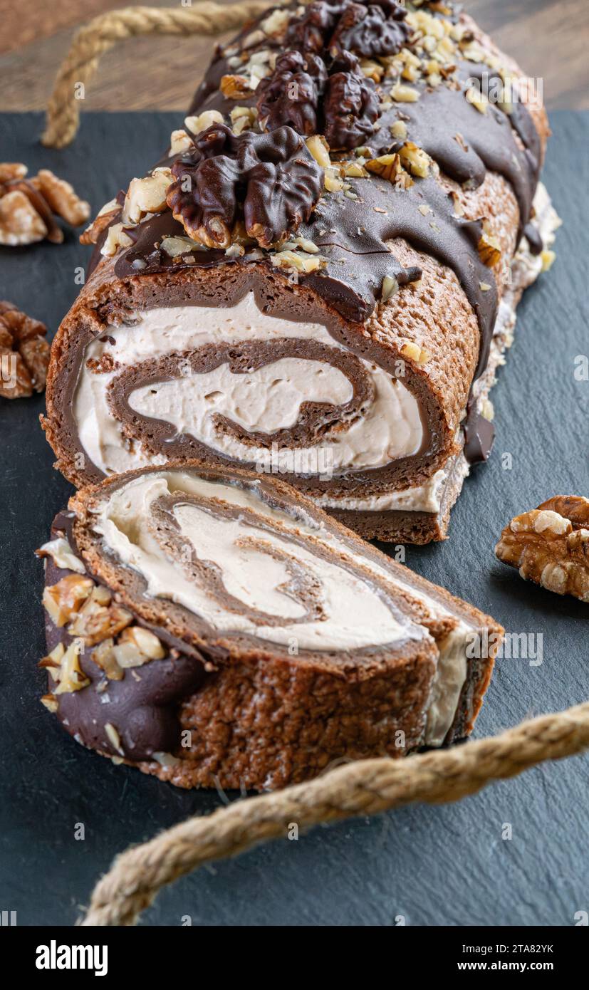 Ein Schweizer Brötchen in Scheiben geschnitten und garniert mit dunkler Schokolade, Haselnüssen und Buttercremefüllung auf Holzschiefer. Perfekt für jeden Tag oder Neujahr. Stockfoto