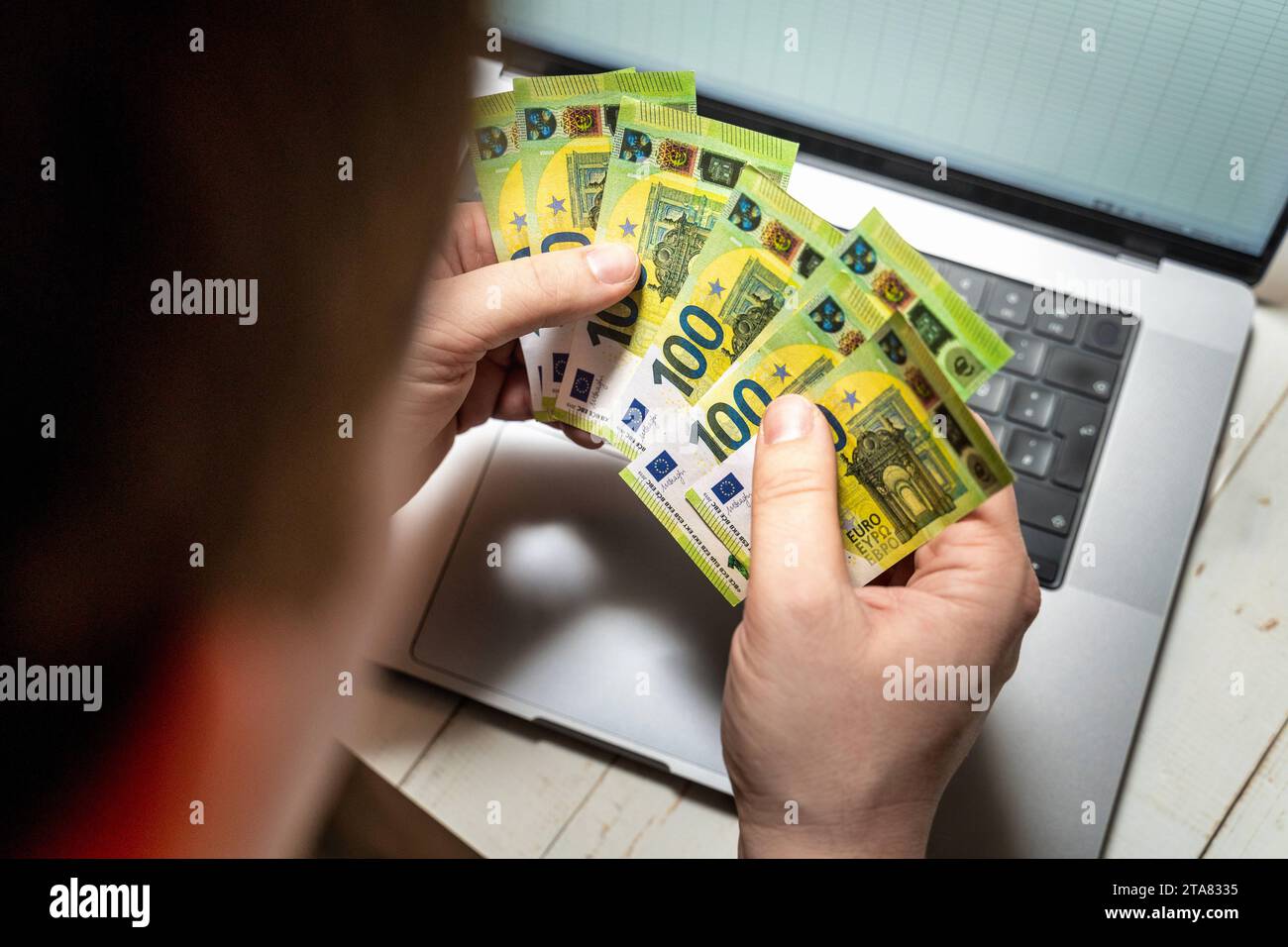 24. November 2023: Ein Mann hält mehrere 100-Euro-Banknoten vor seinem Laptop *** ein Mann hält mehrere 100 Euro Geldscheine vor seinem Laptop Stockfoto