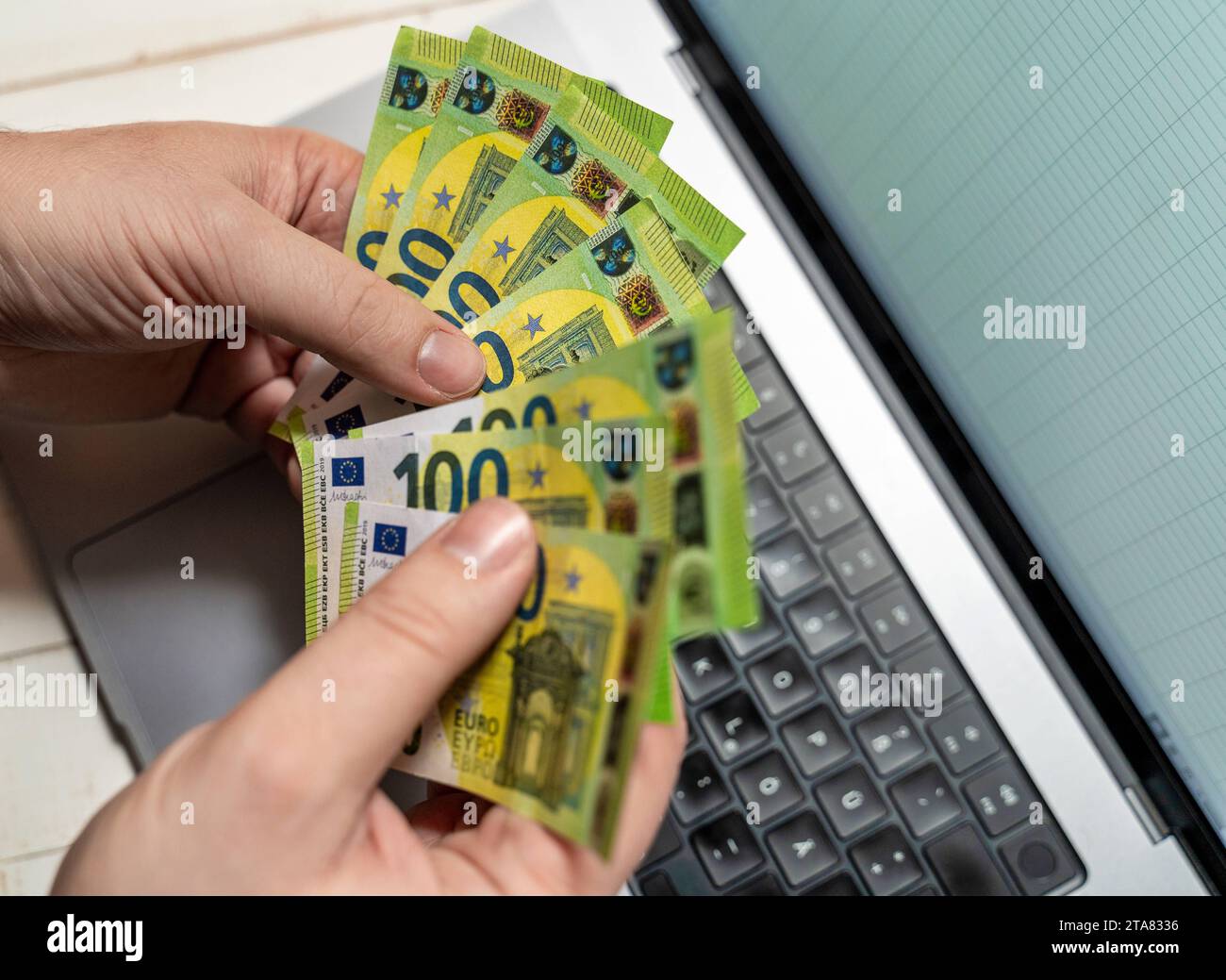 24. November 2023: Ein Mann hält mehrere 100-Euro-Banknoten vor seinem Laptop *** ein Mann hält mehrere 100 Euro Geldscheine vor seinem Laptop Stockfoto