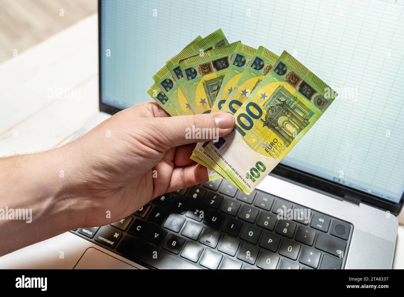 24. November 2023: Ein Mann hält mehrere 100-Euro-Banknoten vor seinem Laptop *** ein Mann hält mehrere 100 Euro Geldscheine vor seinem Laptop Stockfoto