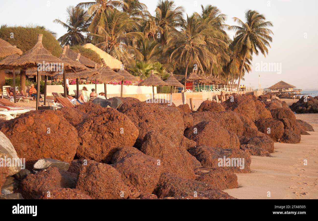 Am Strand, Saly-Portudal, Petite Côte von Senegal, Senegal. Strand, Liegestühle, Bäume, Strohdächer, Schatten am Strand, Felsen, Sonnenbaden Stockfoto