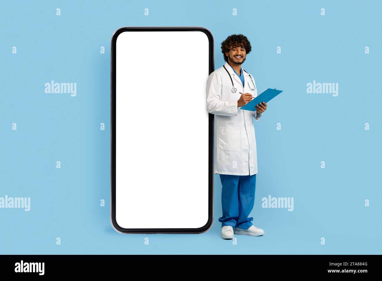 Junger indischer Doktor, der neben einem riesigen Telefon steht Stockfoto