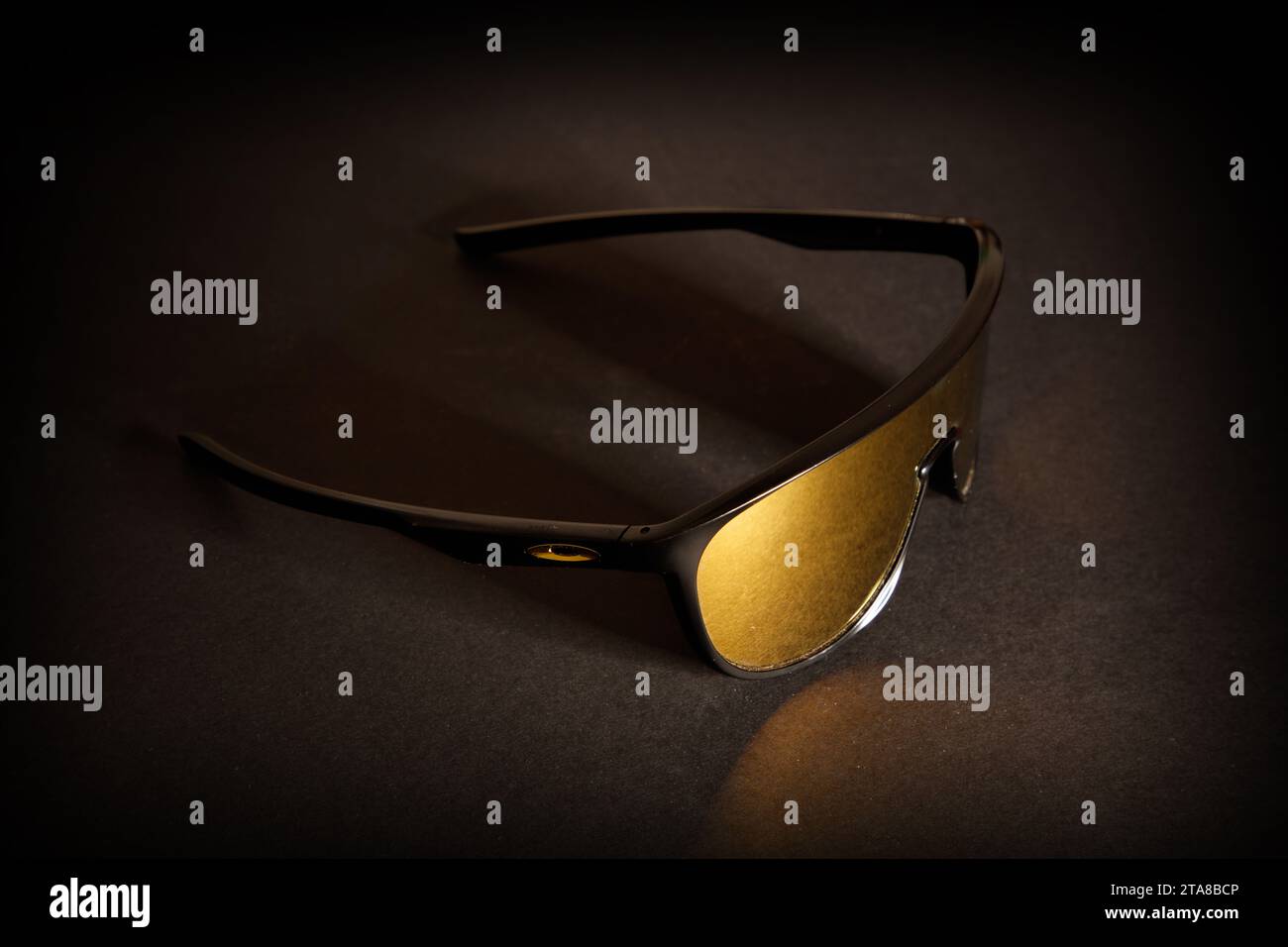 Eine fantastische Studioaufnahme einer sportlichen Oakley Sonnenbrille mit goldener Linse vor dunklem schwarzem Hintergrund Stockfoto