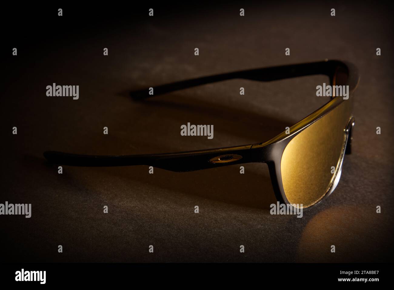 Eine fantastische Studioaufnahme einer sportlichen Oakley Sonnenbrille mit goldener Linse vor dunklem schwarzem Hintergrund Stockfoto