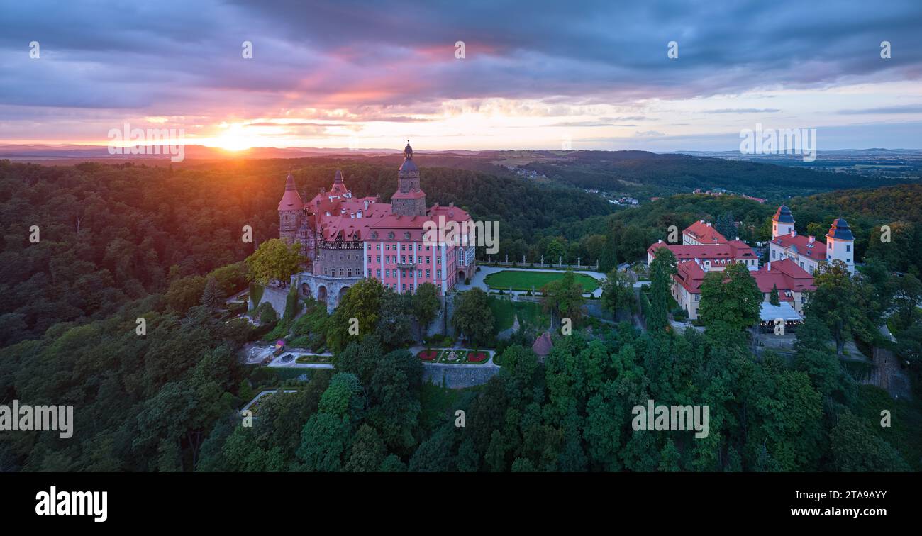 Roter Sonnenuntergang über Schloss Ksiaz, Schloss Fürstenstein, ein wunderschönes Schloss auf einem Felsen, umgeben von Wald. Luftaufnahme, Panoramaaufnahme. Stockfoto