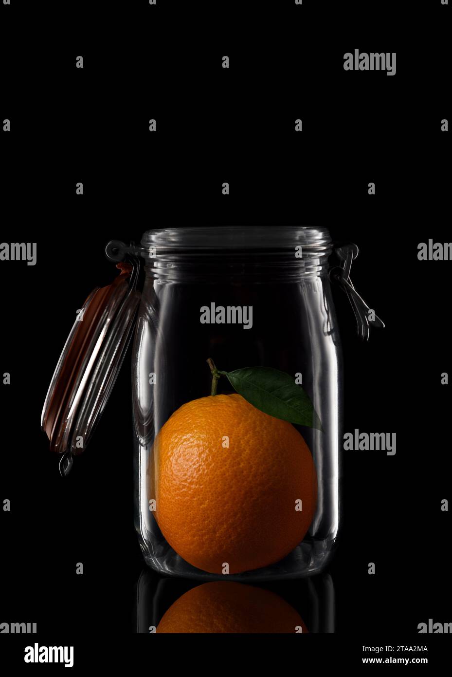 Orange mit Stiel und Blatt in einem Glasbehälter oder Dosenbecher isoliert auf Schwarz mit Reflexion, mit offenem Deckel. Stockfoto