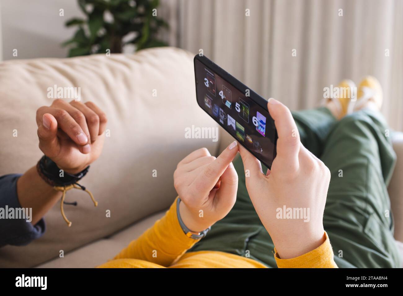 Diverse Paare, die auf der Couch liegen und das Smartphone im Wohnzimmer zu Hause nutzen, Kopierraum. Liebe, Zweisamkeit, Technologie, Kommunikation und häusliches Leben Stockfoto