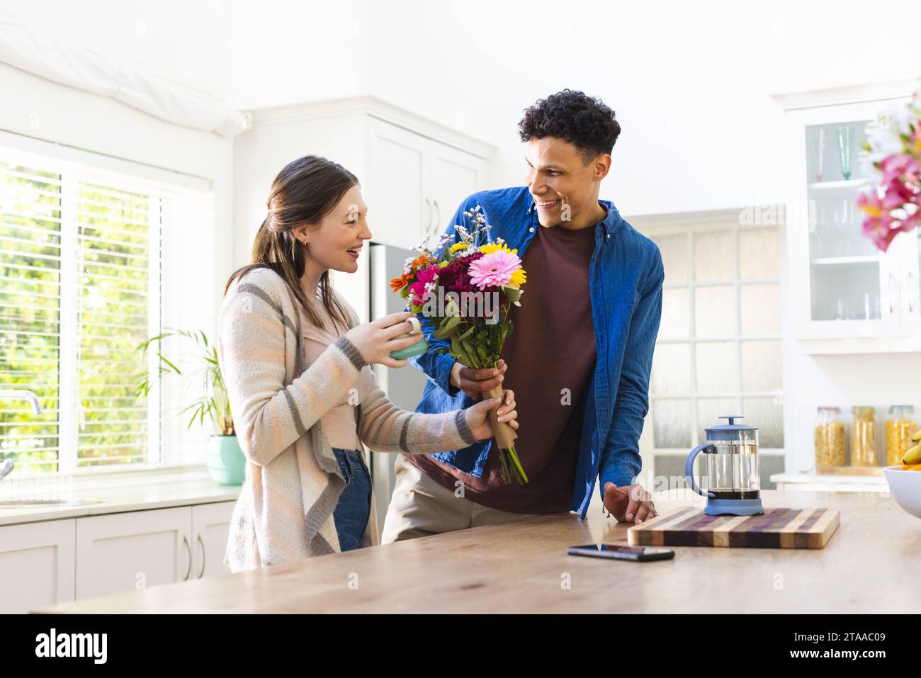 Glückliches, vielfältiges Paar mit Blumen und Teetasse in der Küche zu Hause, Kopierraum. Ausdruck, Liebe, Zweisamkeit, Pflanze, Geschenk, Essen und Trinken A Stockfoto