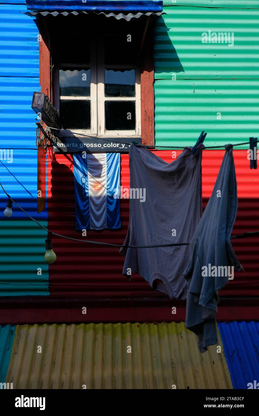 Eine argentinische Flagge und Wäschereien hängen vor einem bunten Häuserfenster in La Boca. Buenos Aires. Argentinien Stockfoto