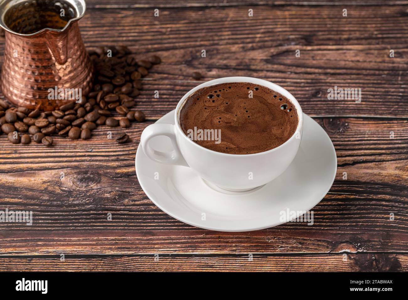 Doppelter türkischer Kaffee in einer weißen Porzellantasse mit dekorativer Kaffeekanne auf einem Holztisch Stockfoto