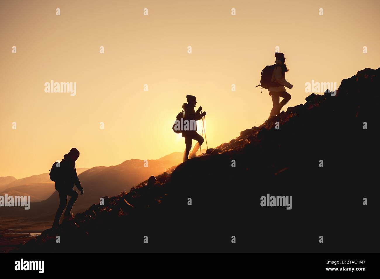 Gruppe von Wanderern mit Rucksäcken geht bergauf in den Sonnenuntergang Bergen Stockfoto