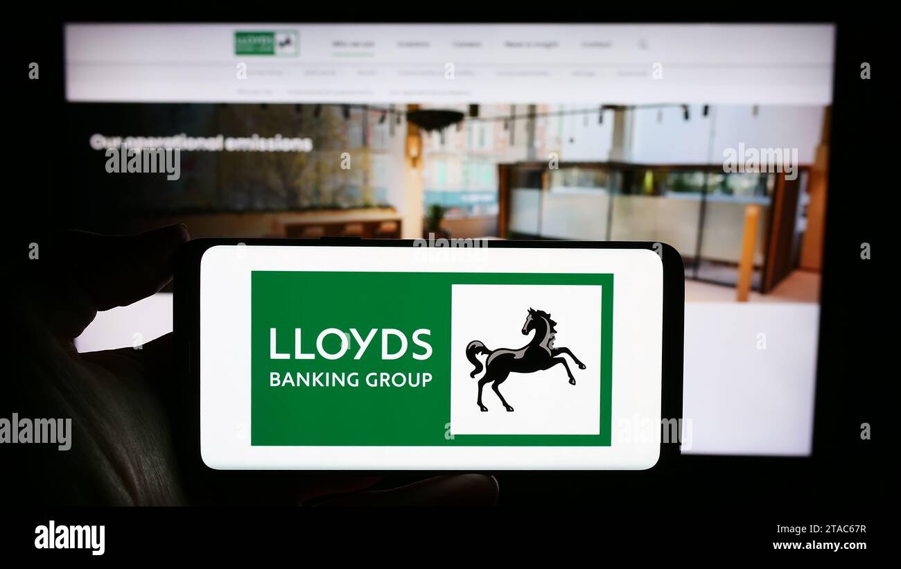 Person mit Smartphone und Logo des britischen Finanzunternehmens Lloyds Banking Group plc vor der Website. Schwerpunkt auf dem Display des Telefons. Stockfoto