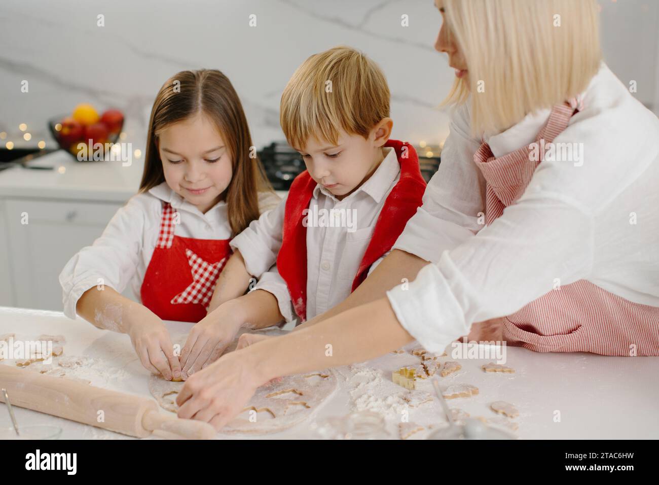 Eine Mutter bringt ihrer Tochter und ihrem kleinen Sohn bei, wie man Kekse macht. Eine Frau und ihre Kinder bereiten Weihnachtskekse mit einer Teigform zu. Stockfoto