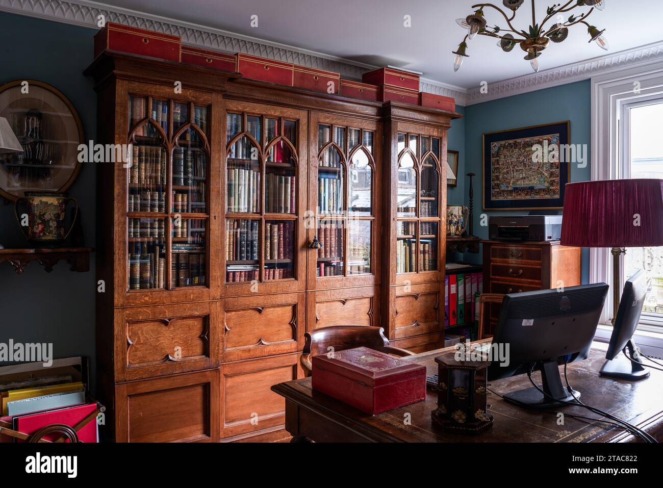 Antikes Bücherregal und Schreibtisch mit Computerbildschirm im West London Haus des späten 19. Jahrhunderts. Stockfoto