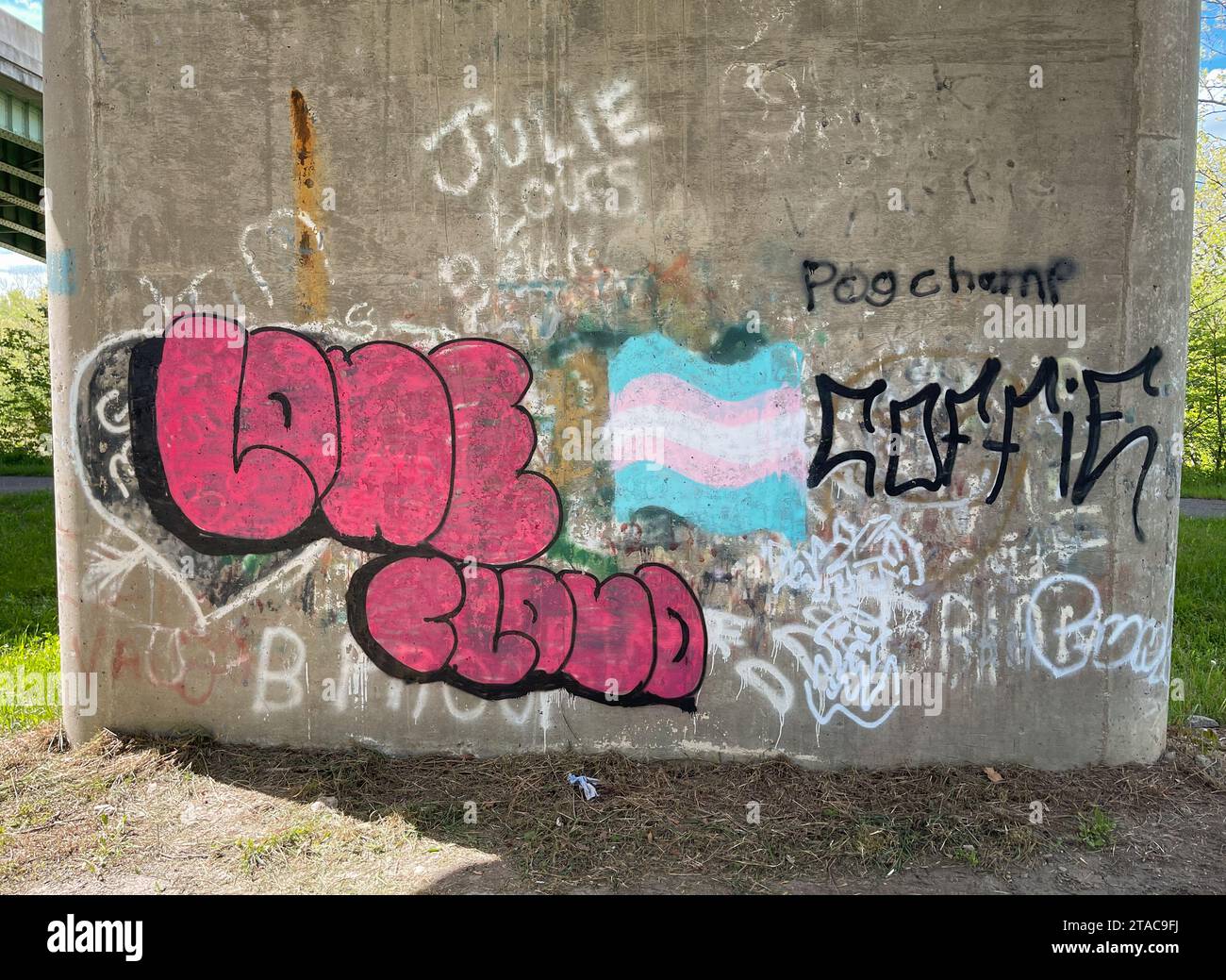 Ein Betonpfeiler einer Brücke ist mit Blasenbuchstaben-Graffiti, einem pastellfarbenen flaggenartigen Gemälde und schwarzen Tags am Hockhocking Adena Bikeway in Athens, Ohio, bedeckt. Stockfoto