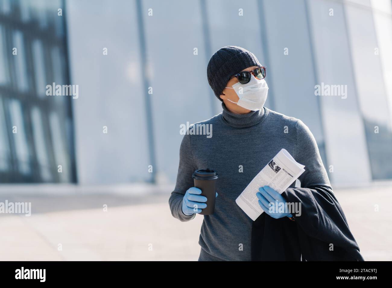 Mann in Winterkleidung mit Kaffeetasse und Zeitung, Handschuhe und Maske Stockfoto