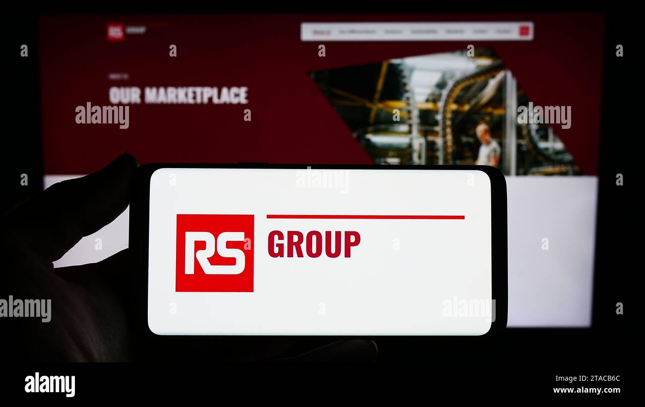 Person mit Smartphone und Logo der britischen Stromverteilerfirma RS Group plc vor der Website. Schwerpunkt auf dem Display des Telefons. Stockfoto