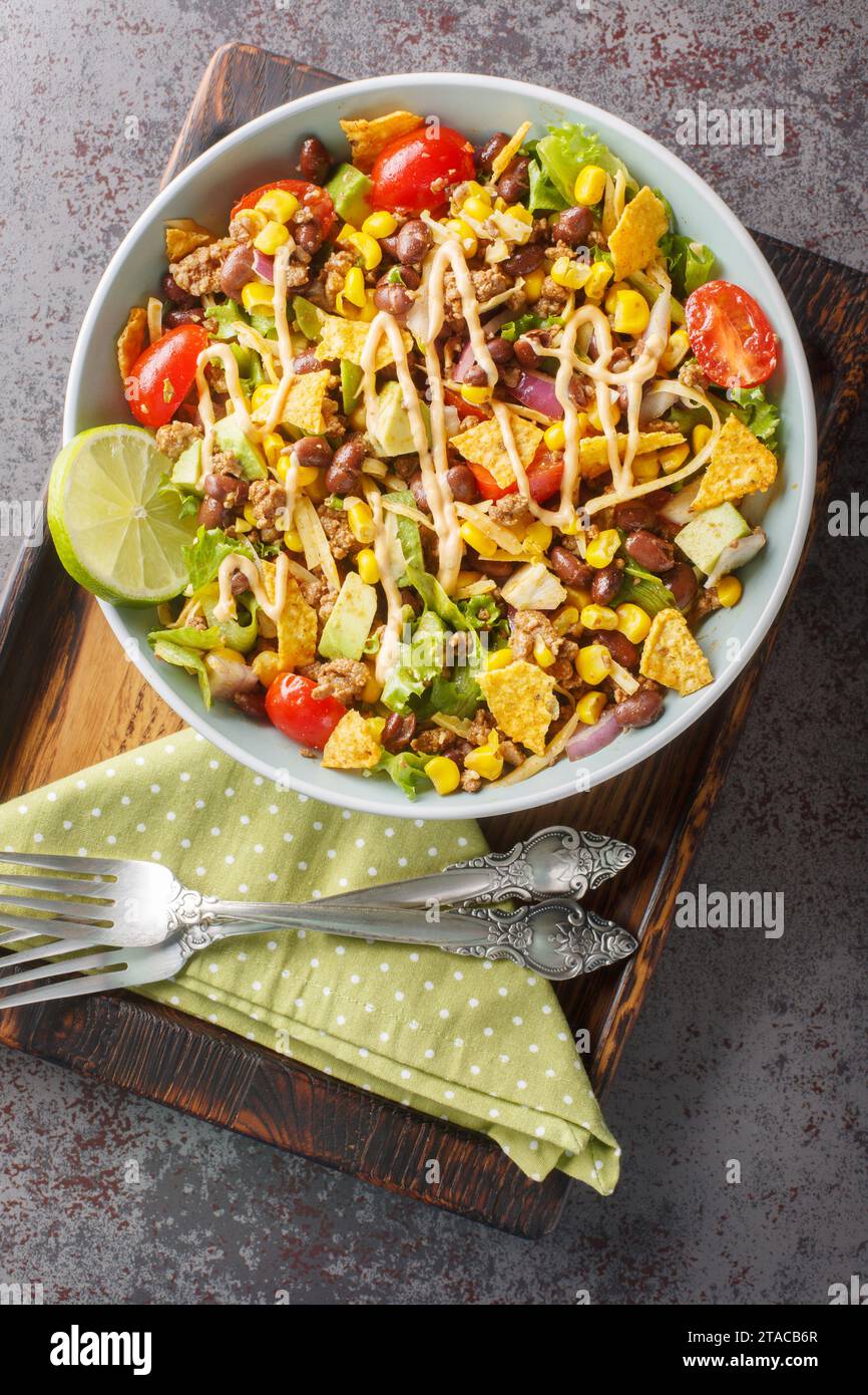 Taco Salat ist ein warmer Salat mit Chili-Bohnen, scharfem Hackfleisch, Mais, Salat, Käse und Avocado aus der Nähe auf dem Teller auf dem Tisch. Vertikal oben Stockfoto