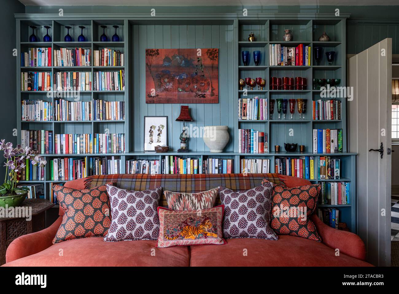 Bücherregale mit blauer Zunge und Groove mit orangefarbenem Sofa in einem Haus im Arts and Crafts Stil der 1930er Jahre. Hove, East Sussex, Großbritannien. Stockfoto