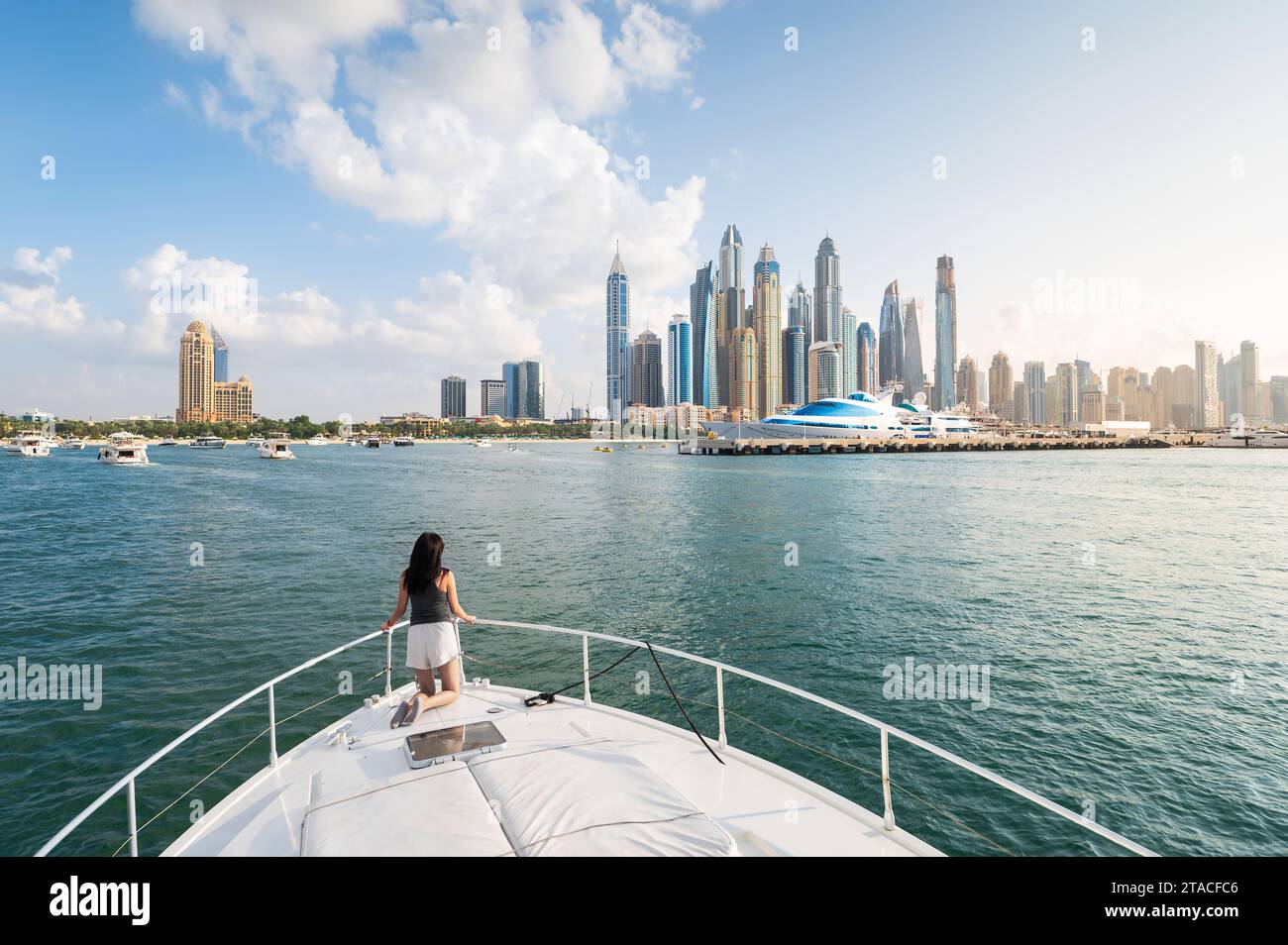 Die bezaubernde Schönheit der Marina von Dubai, während eine stilvolle Frau den ruhigen Sonnenuntergang während einer luxuriösen Yachtfahrt umarmt. Das Wesen der Raffinesse einfangen Stockfoto