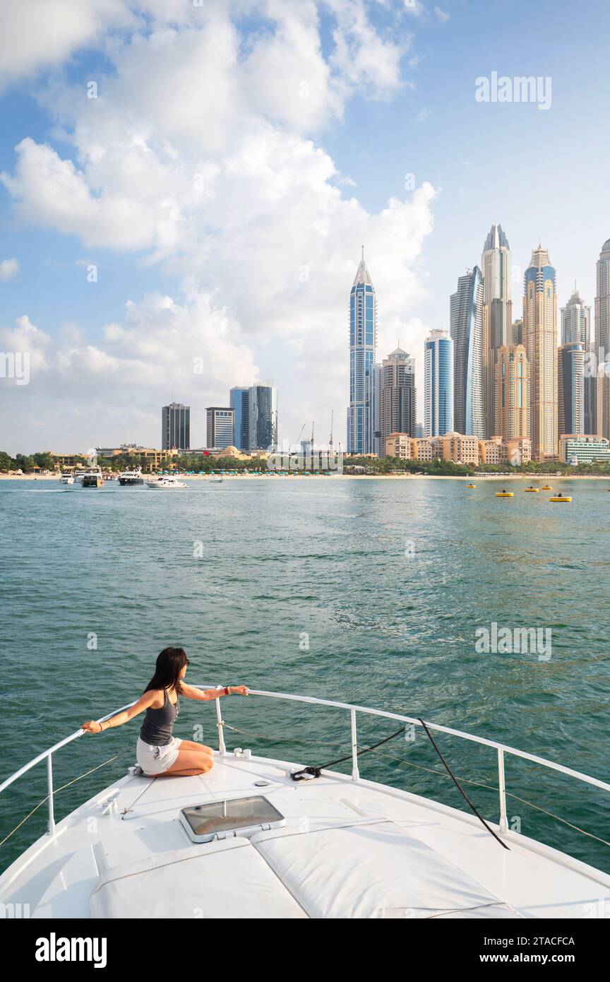 Die bezaubernde Schönheit der Marina von Dubai, während eine stilvolle Frau den ruhigen Sonnenuntergang während einer luxuriösen Yachtfahrt umarmt. Das Wesen der Raffinesse einfangen Stockfoto