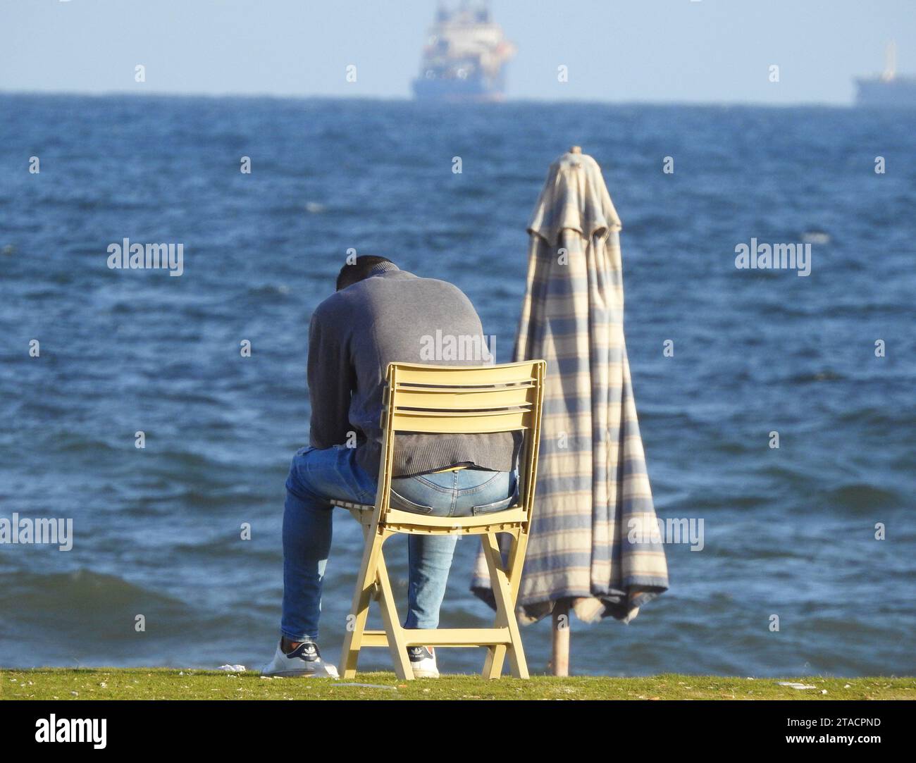 Ein junger Mann von hinten, der allein auf einem Stuhl am Ufer des Mittelmeers sitzt, unerkannte Person, die am Strand sitzt, Depression, ich Stockfoto