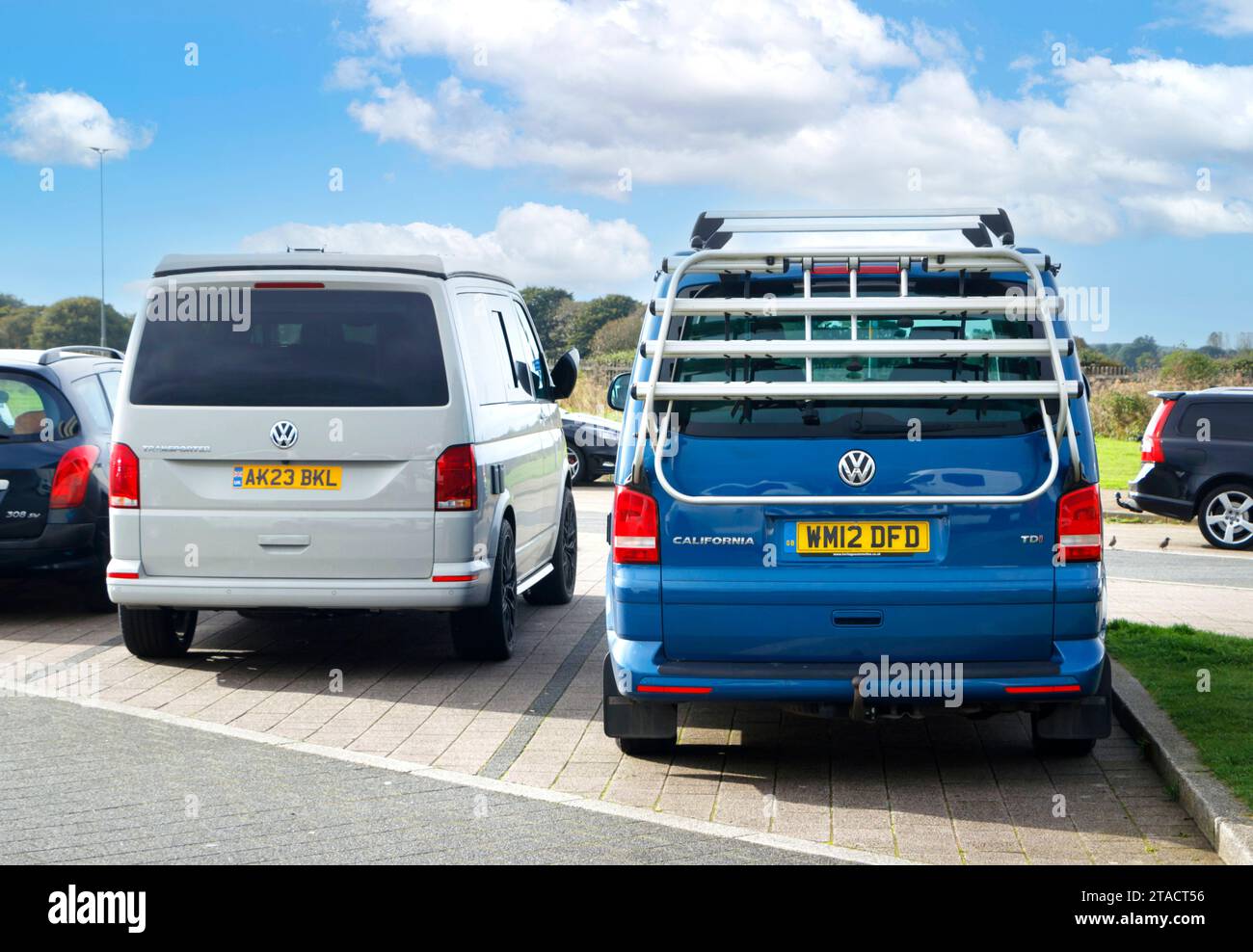 T6 T6.1 Volkswagen Wohnmobil in Ascot Grey mit aufklappbarem Dach neben blauem VW California Wohnmobil mit Fahrradträger Stockfoto