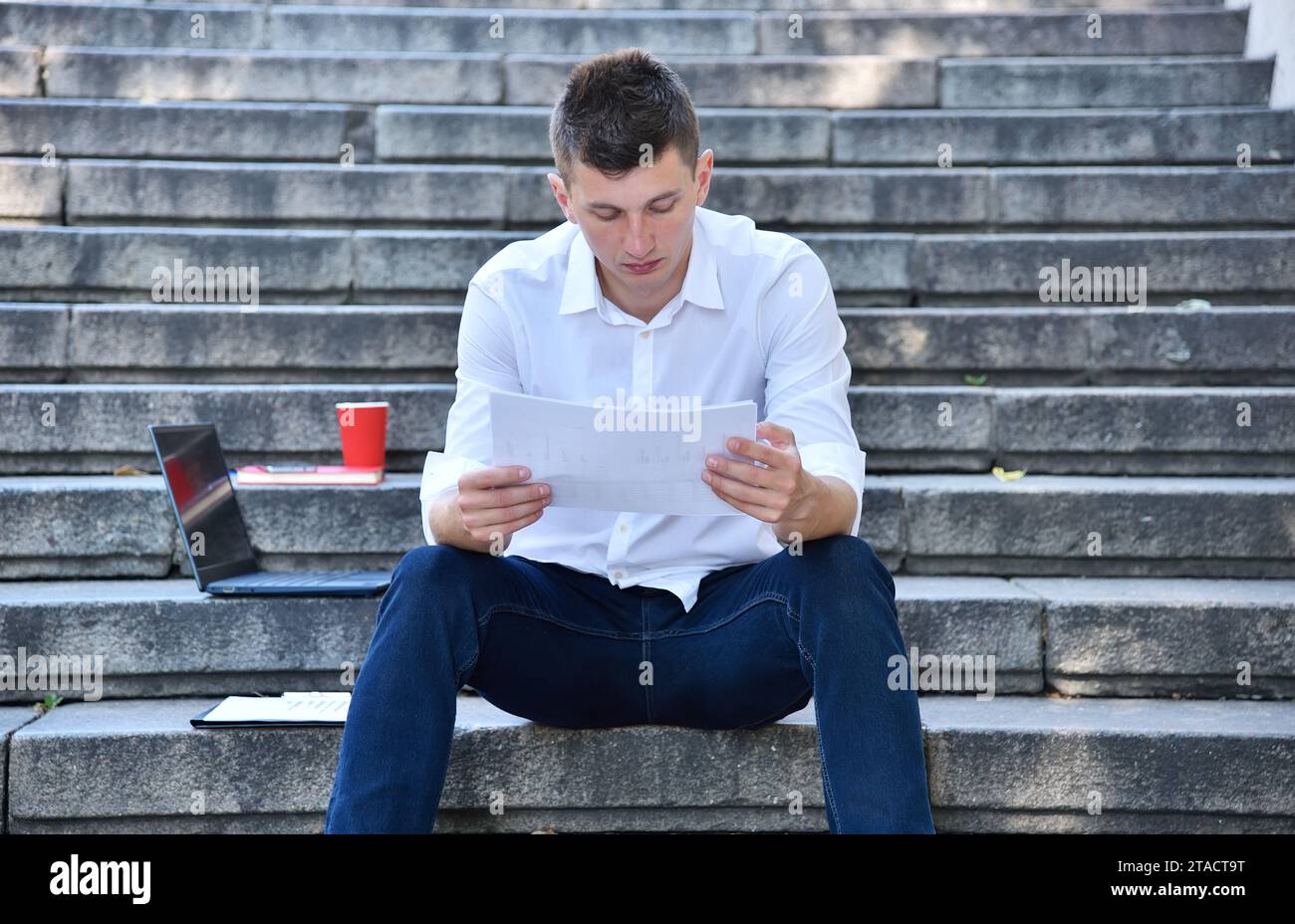 Geschäftsmann sitzt auf der Treppe und sieht sich den Finanzbericht an. Geschäfts- und Handelskonzept. Stockfoto